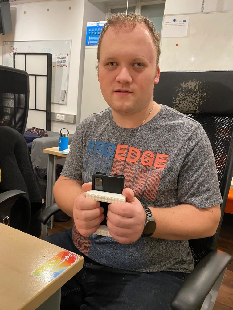 Jugendlicher mit den Händen auf Rechteck aus Klemmbausteinen auf einem Smartphone vor dem Körper haltend.