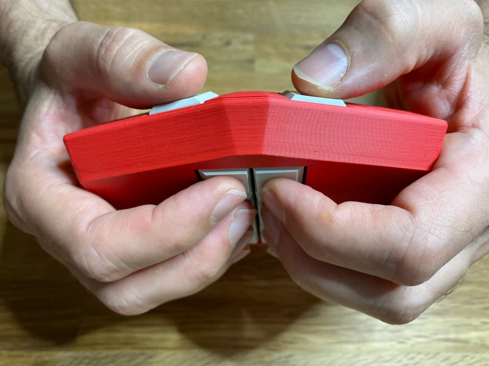 Hände halten die mobile Braille-Tastatur Metabraille. Das Tastaturgehäuse ist rot und aus Kunststoff (125 mm x 95 mm x 25 mm). Die zehn Tasten sind weiß und rechteckig. Rechteckig ist auch die Gehäuseform, mit einer flachen, trapezförmigen Erweiterung auf der Längsseite. Die Tastatur liegt in zwei Handflächen, die Finger liegen auf acht Tasten auf der flachen Vorderseite und die Daumen liegen oben auf der gegenüberliegenden Seite auf zwei Tasten.