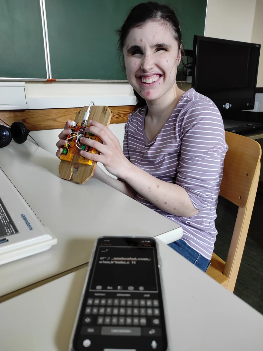 Schülerin mit einem elektronischen Versuchsaufbau einer Tastatur. Smartphone liegt im Vordergrund und zeigt ein Textfeld und die virtuelle Tastatur am Bildschirm.